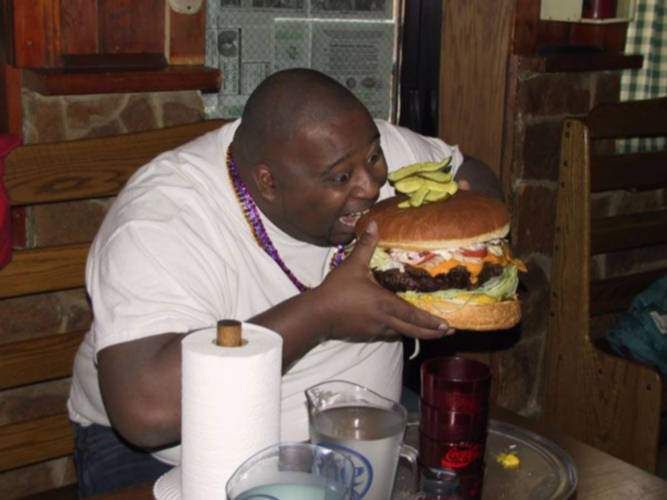 Very fat man eating a huge hamburger note the pile of pickles on TOP of the 